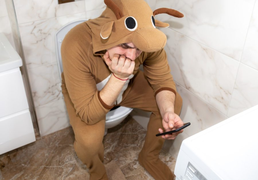 man-cosplay-costume-cow-guy-funny-animal-pyjamas-sit-toilet-playing-games-mobile-phone